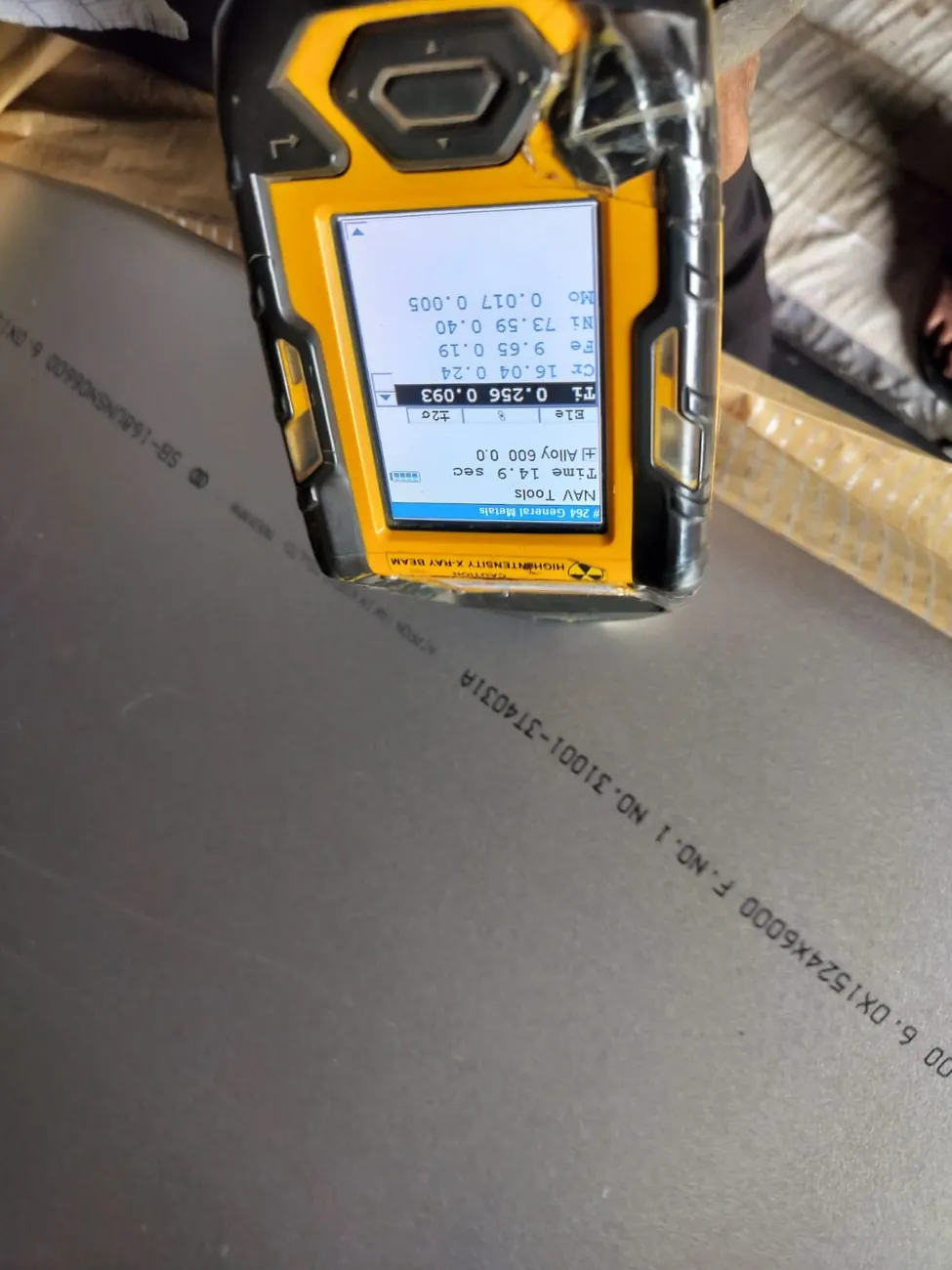 Handheld XRF analyser resting on an Alloy 600 plate beside its rolled marking